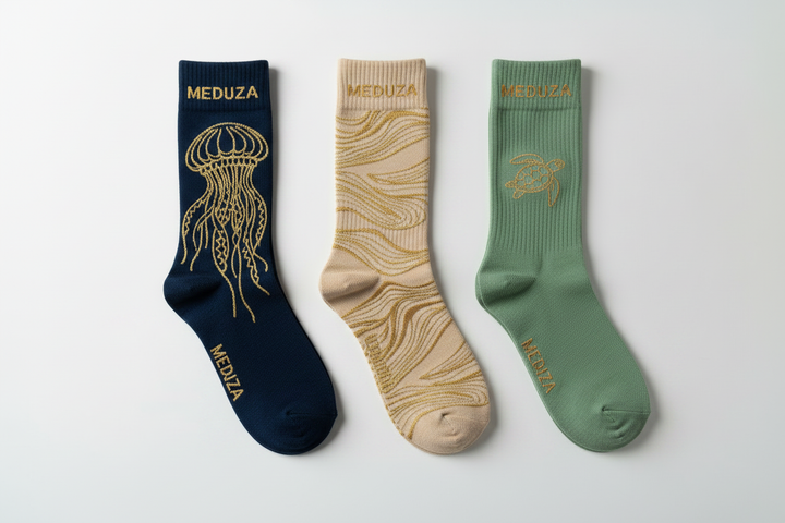 Three pairs of Meduza luxury crew socks in navy, beige, and sage green with gold ocean graphics